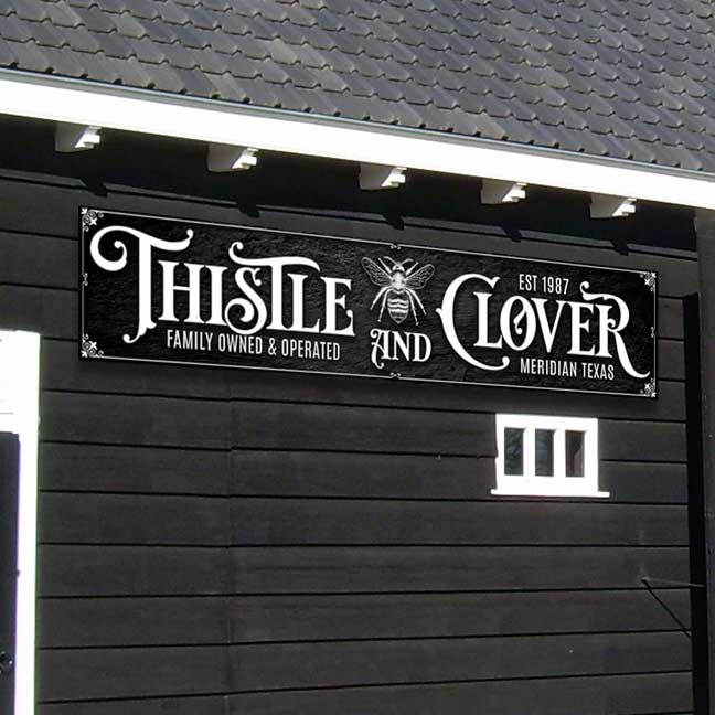Custom barn sign on black texture with white fancy font that says Thistle and Clover