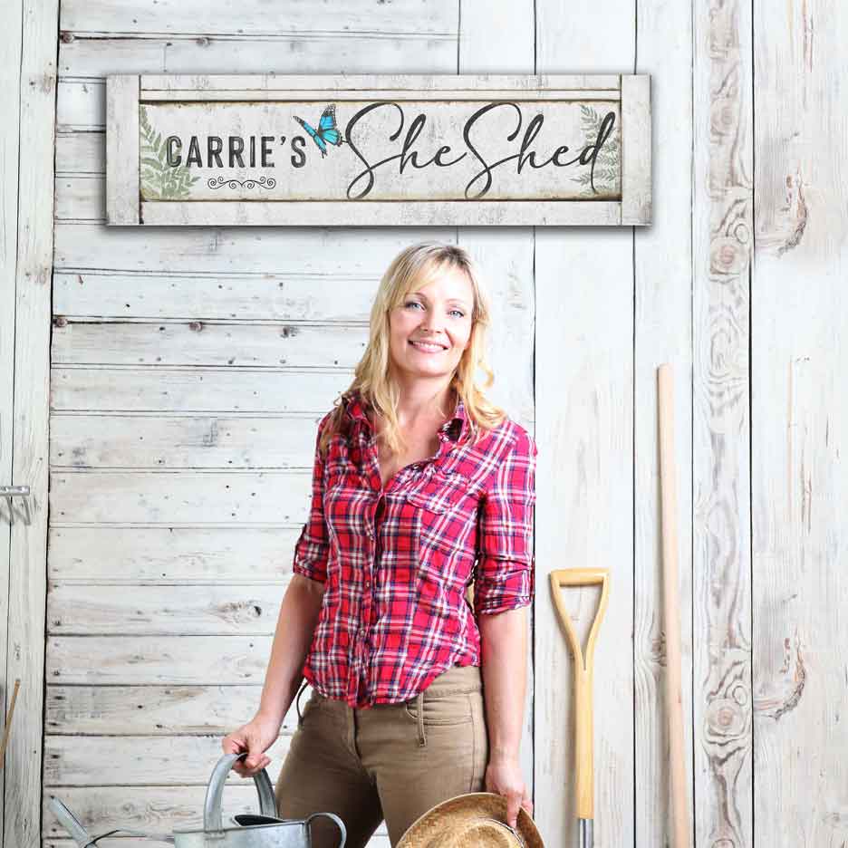 White Metal She Shed Sign Personalized on a white barn with a rustic wood faux frame that says Carries She Shed