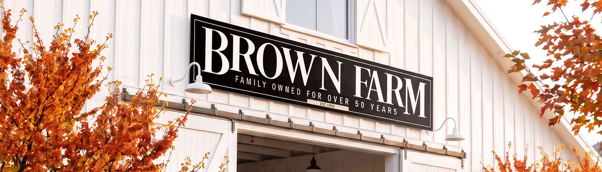 Personalized metal barn sign reading Brown Farm, family owned for over 50 years, est 1976, mounted above a white barn door under gooseneck lights in autumn