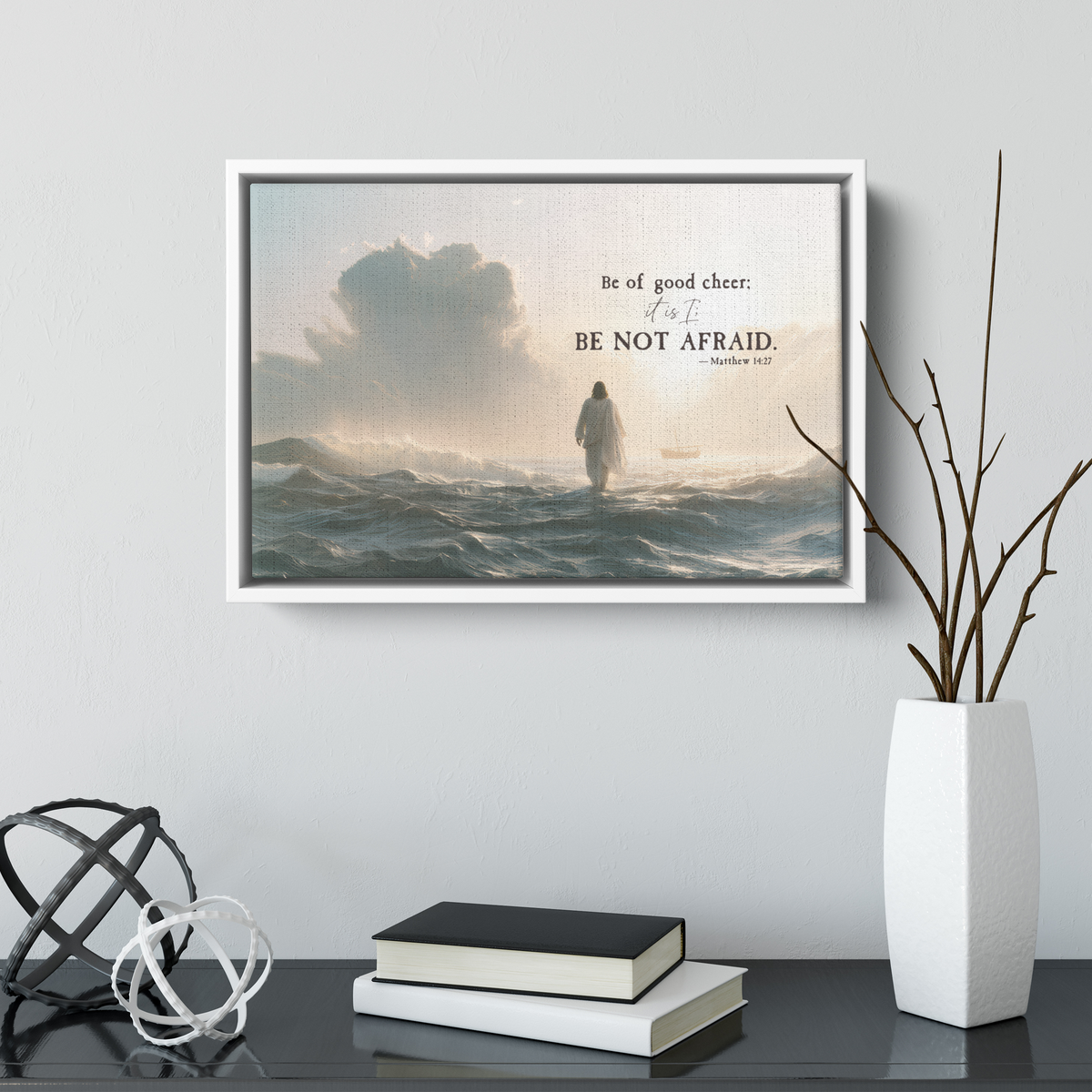 Smaller Be Not Afraid canvas in a white frame above a dark console with books and a white vase of branches