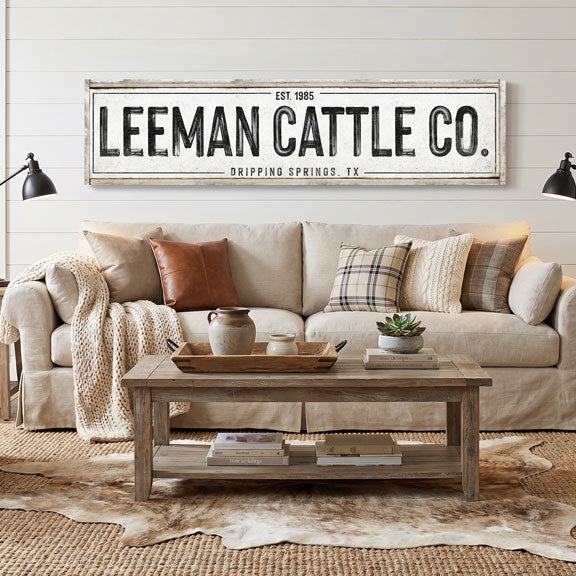 Living room with a beige sofa, wooden coffee table, and 'Leeman Cattle Co.' canvas cattle ranch sign on the wall.