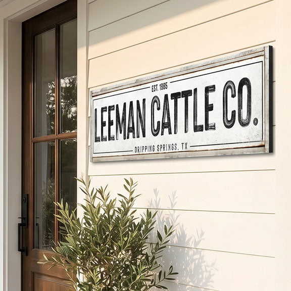 Leeman Cattle Co. cattle ranch sign on a building exterior with a plant in the foreground.