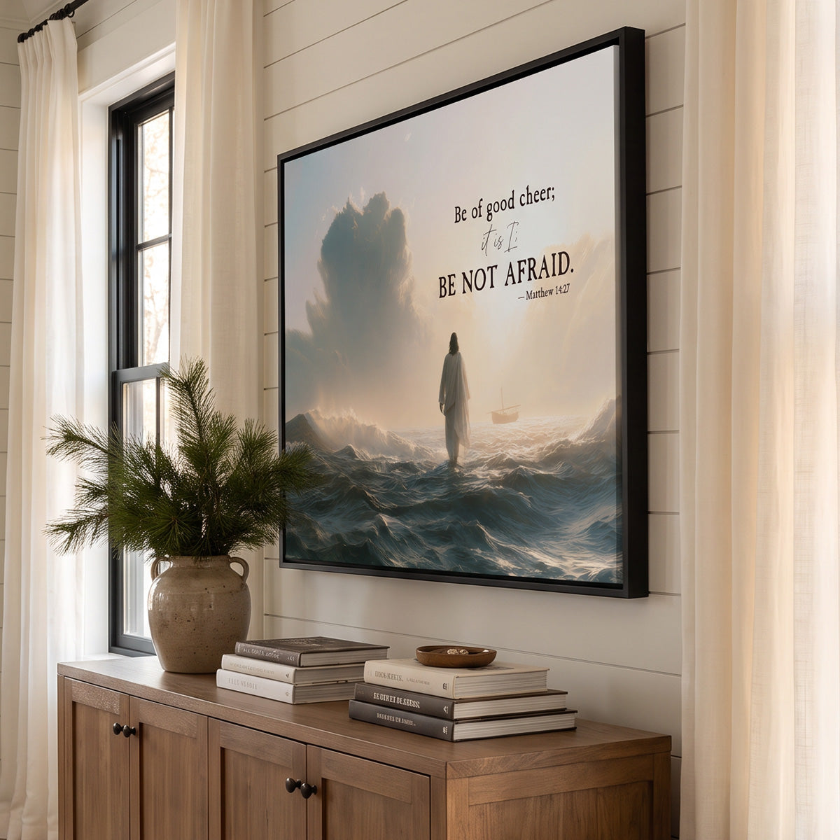 Jesus walking on water canvas in a black floating frame, angled view above an oak sideboard with pine branches and stacked books