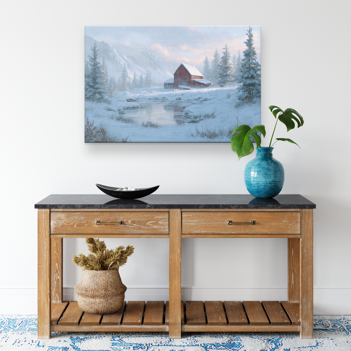Mountain red barn Christmas canvas above a light oak console with a blue vase and a woven basket