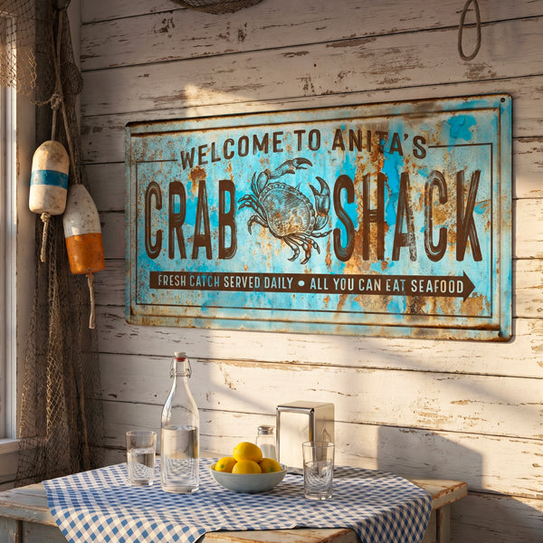 Coastal Wall Art sign reading 'Welcome to Anita's Crab Shack' with a crab illustration, mounted on a whitewashed wood wall above a table with a blue-and-white checkered cloth, glass bottles, and lemons.