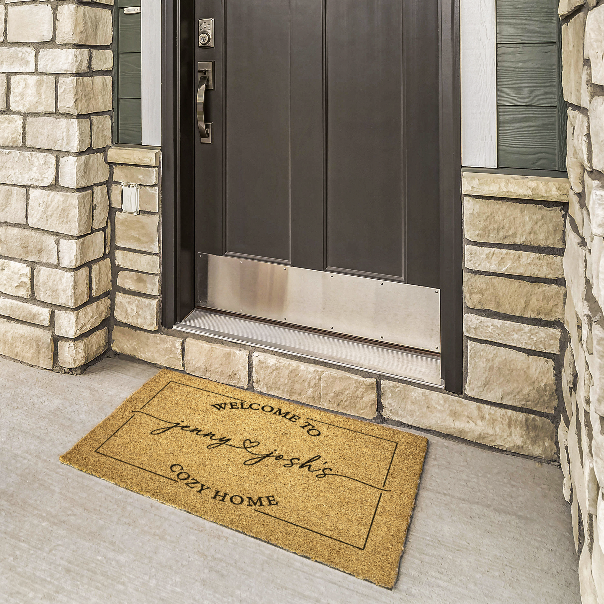 Couples coir welcome mat with first names and a heart at a bronze door framed by cream stone