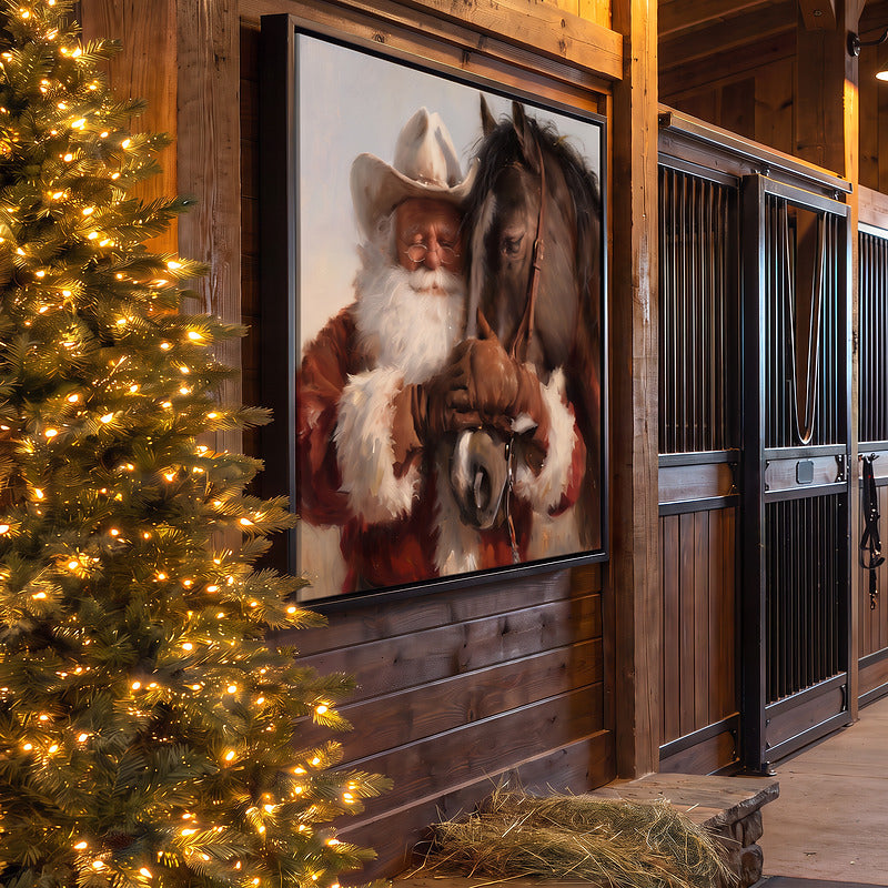 Western Santa and horse canvas in a black frame on a barn wall beside a tall lit Christmas tree and horse stalls