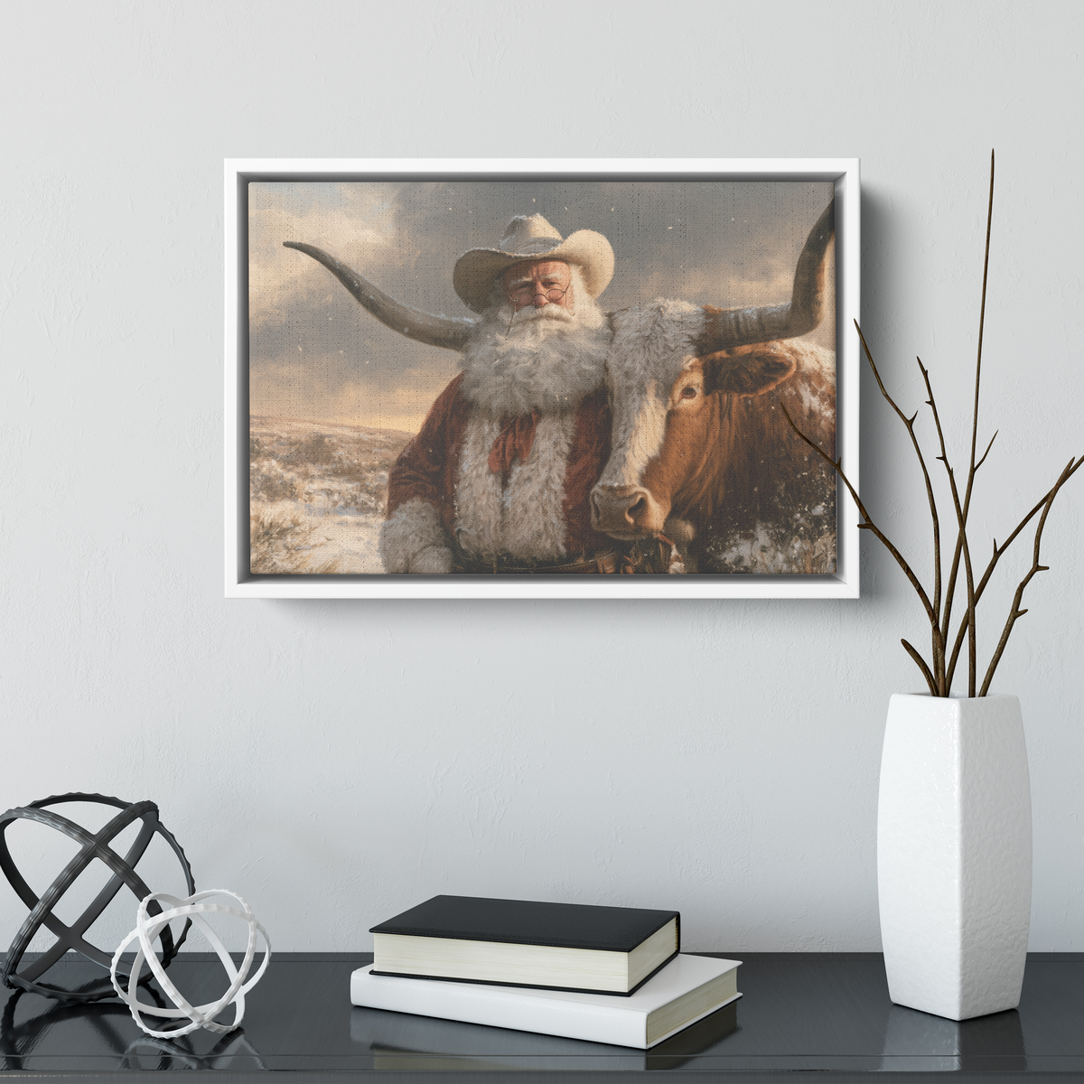 Cowboy Santa and longhorn canvas in a white frame above a dark console with books and a white vase