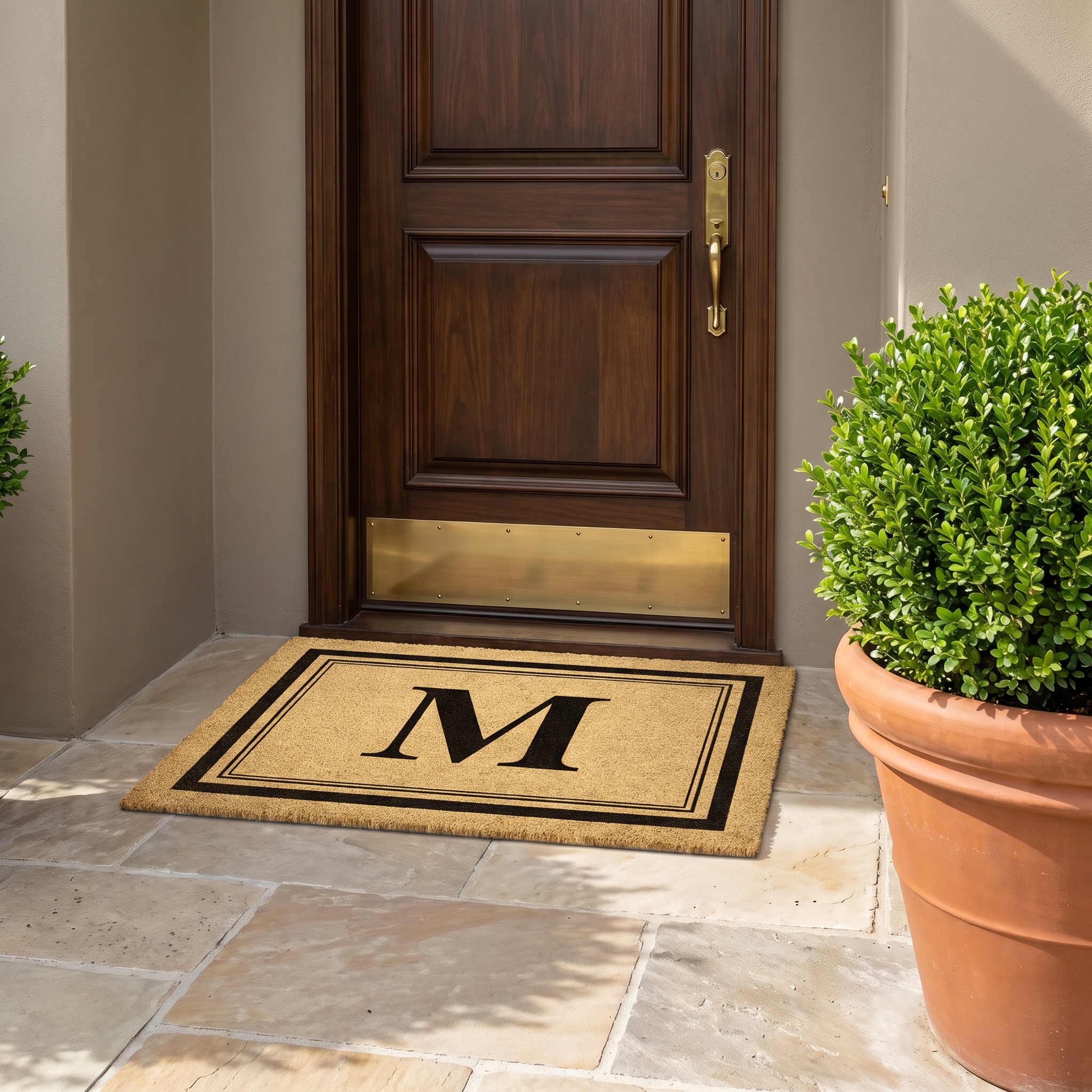 Custom door mat with initial M in black on natural coir at a dark wood entry door with brass kickplate