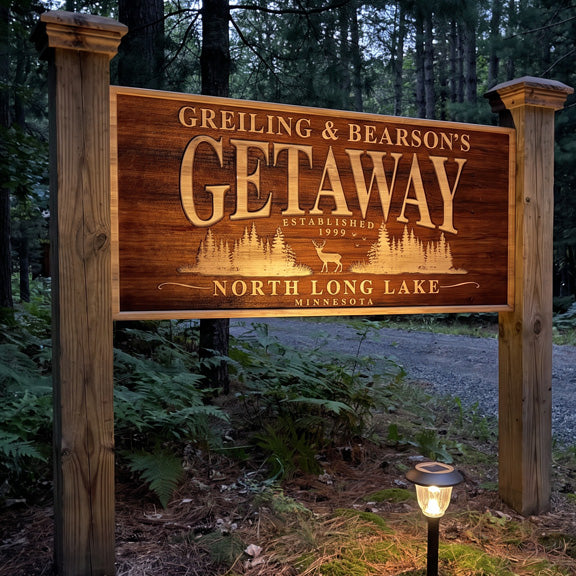 Family name lake getaway sign between posts at a driveway entrance at dusk with a solar path light
