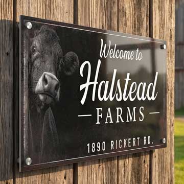 Farm Entrance Sign - Welcome to Halstead Farms with a cow's face on a wooden background
