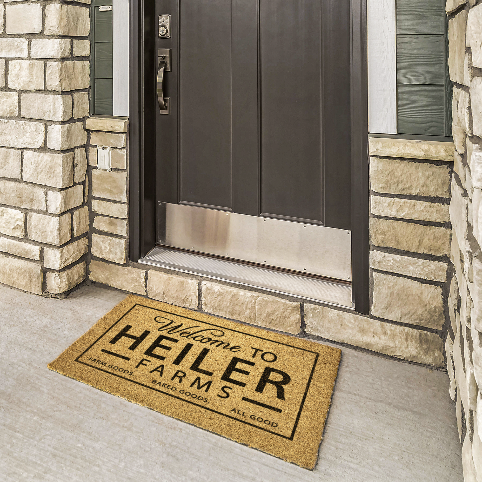 Farmhouse coir welcome mat with farm name at a bronze door framed by cream stone