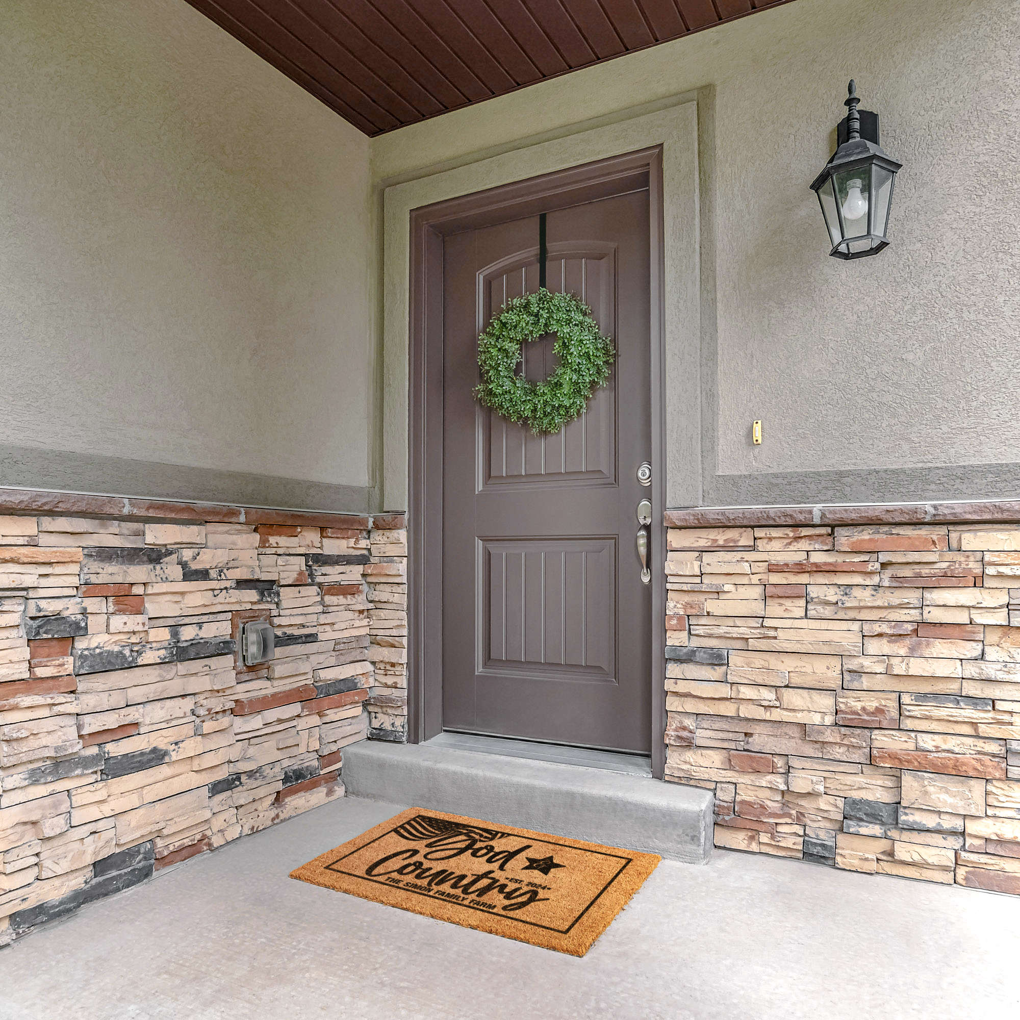 God and Country doormat on a stone porch below a brown door with a green boxwood wreath
