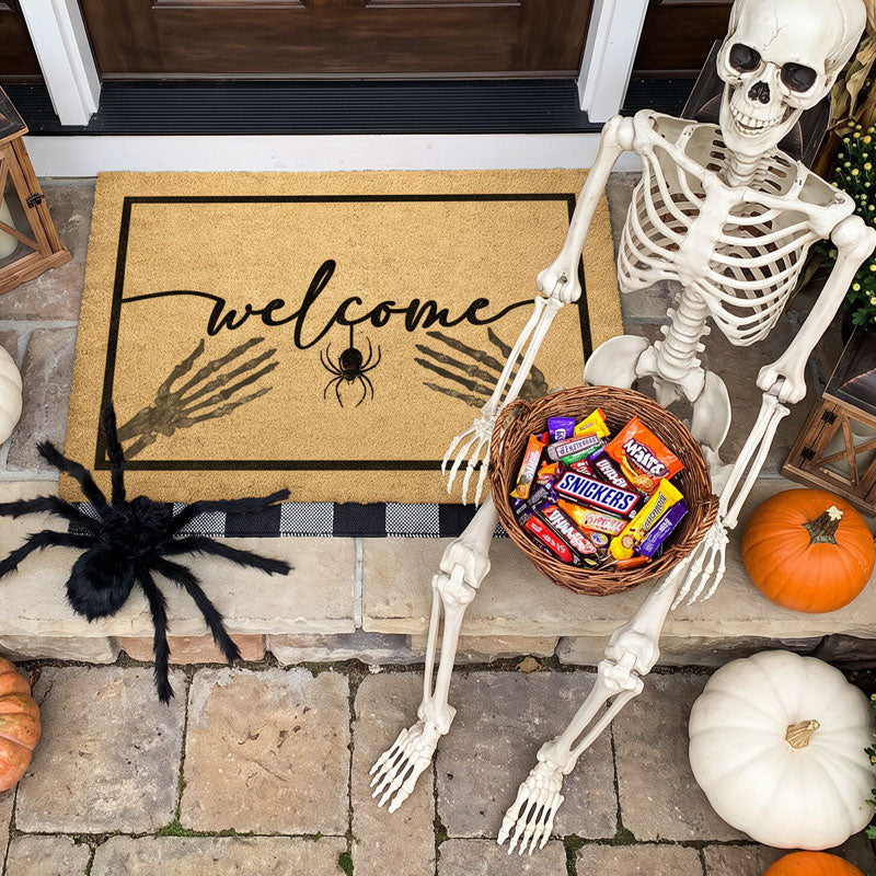 Halloween skeleton doormat reading welcome at a dark door with a black spider and pumpkins