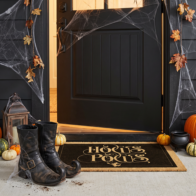 Hocus Pocus Halloween mat at an open black door with cobwebs, boots, a cauldron and small pumpkins