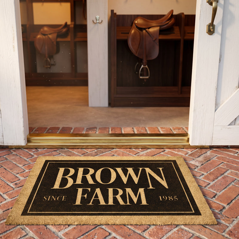 Horse farm welcome mat with farm name and est year on brick, at open barn doors with English saddles on racks
