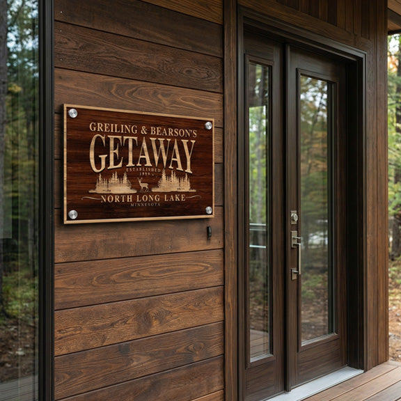 Wood-look metal getaway sign on a stained plank cabin wall beside a glass front door