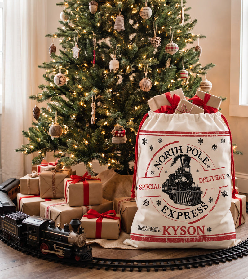 Large fabric Santa sack with a vintage steam train North Pole Express print, filled with gifts by the Christmas tree