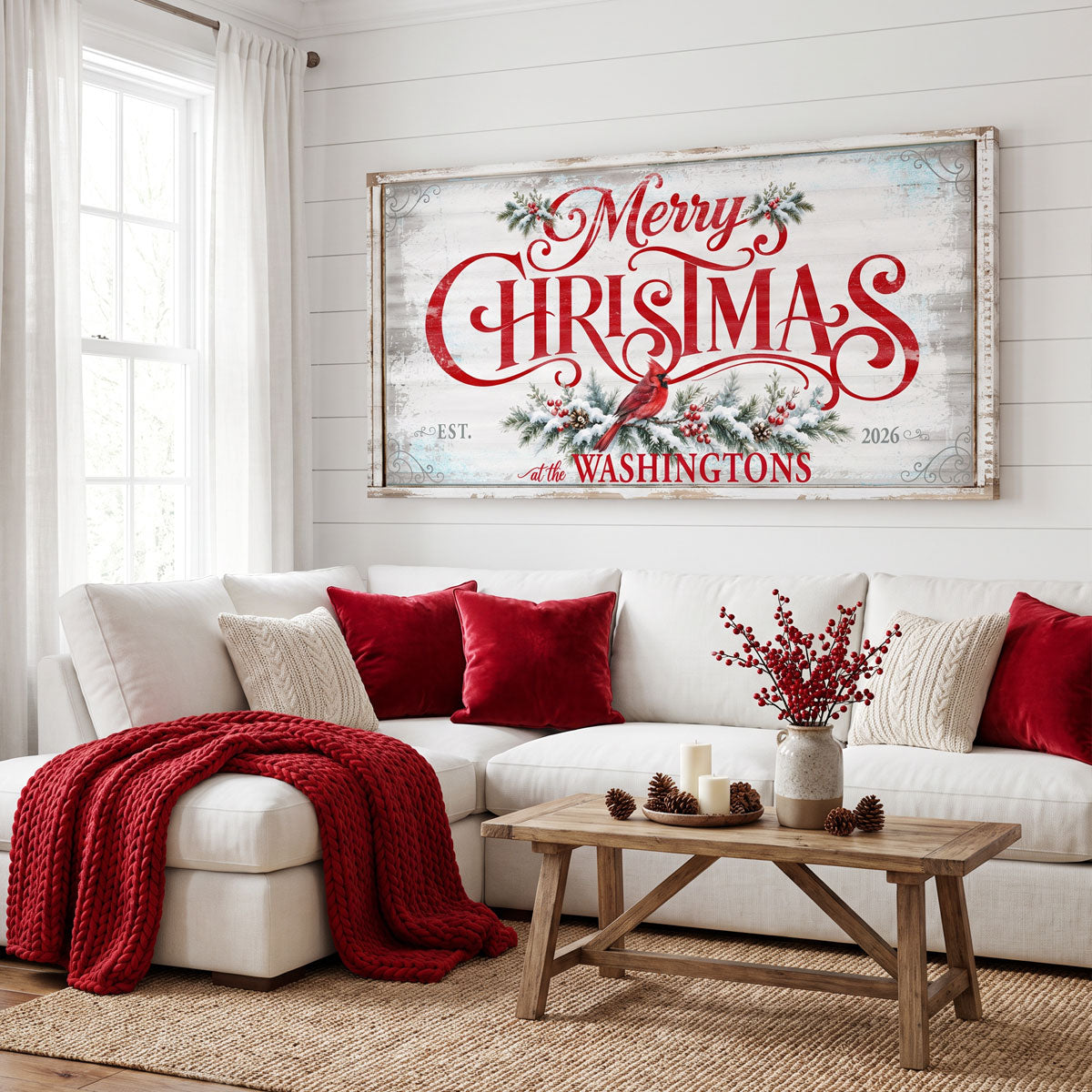 Merry Christmas family name sign above a white sofa with red velvet pillows and a red knit throw