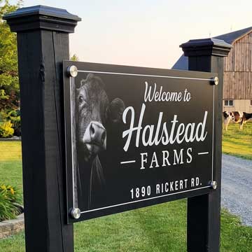 Welcome metal farm sign to Halstead Farms with a cow image on a black background.