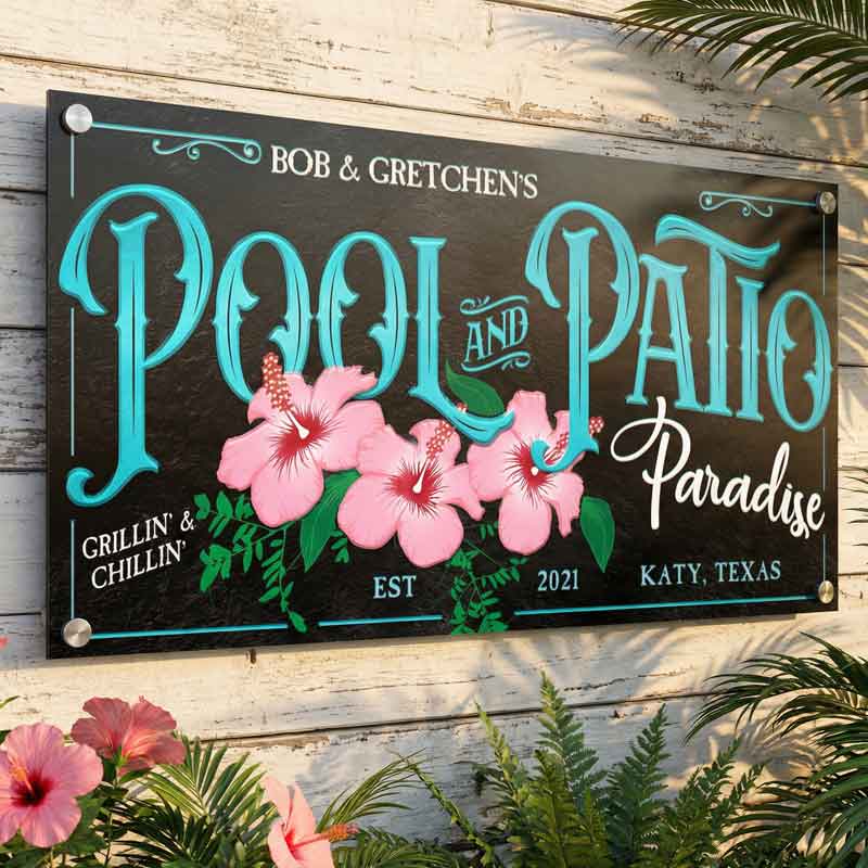 metal pool decor sign in teal and black with pink hibiscus hanging on a wood wall.