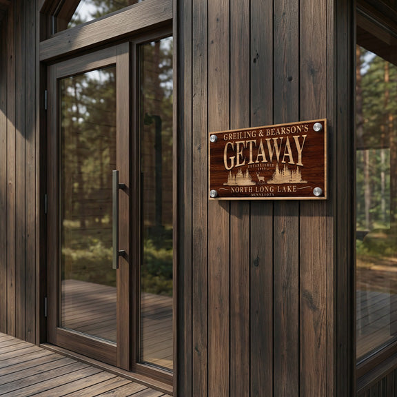 Metal sign that looks like wood mounted on a dark cabin wall beside glass doors at a wooded lake getaway