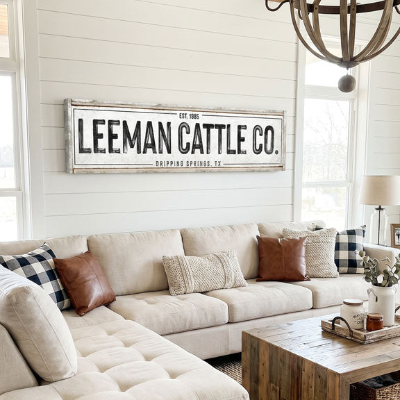 modern farmhouse decor Living room with a 'Leeman Cattle Co.' sign on the wall above a beige sofa.