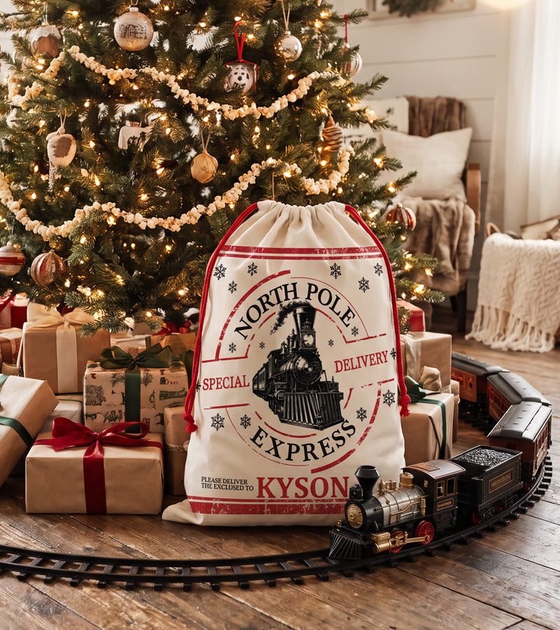 Personalized Christmas gift bag with a North Pole Special Delivery train postmark, beside a toy train set