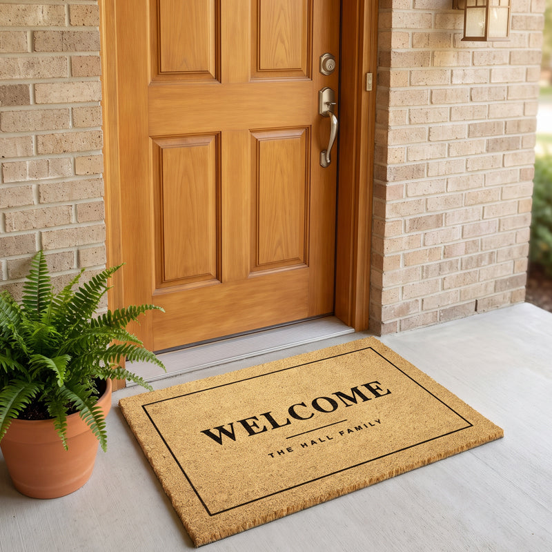 Personalized door mat with family name at a wood door with a fern and a brass wall sconce