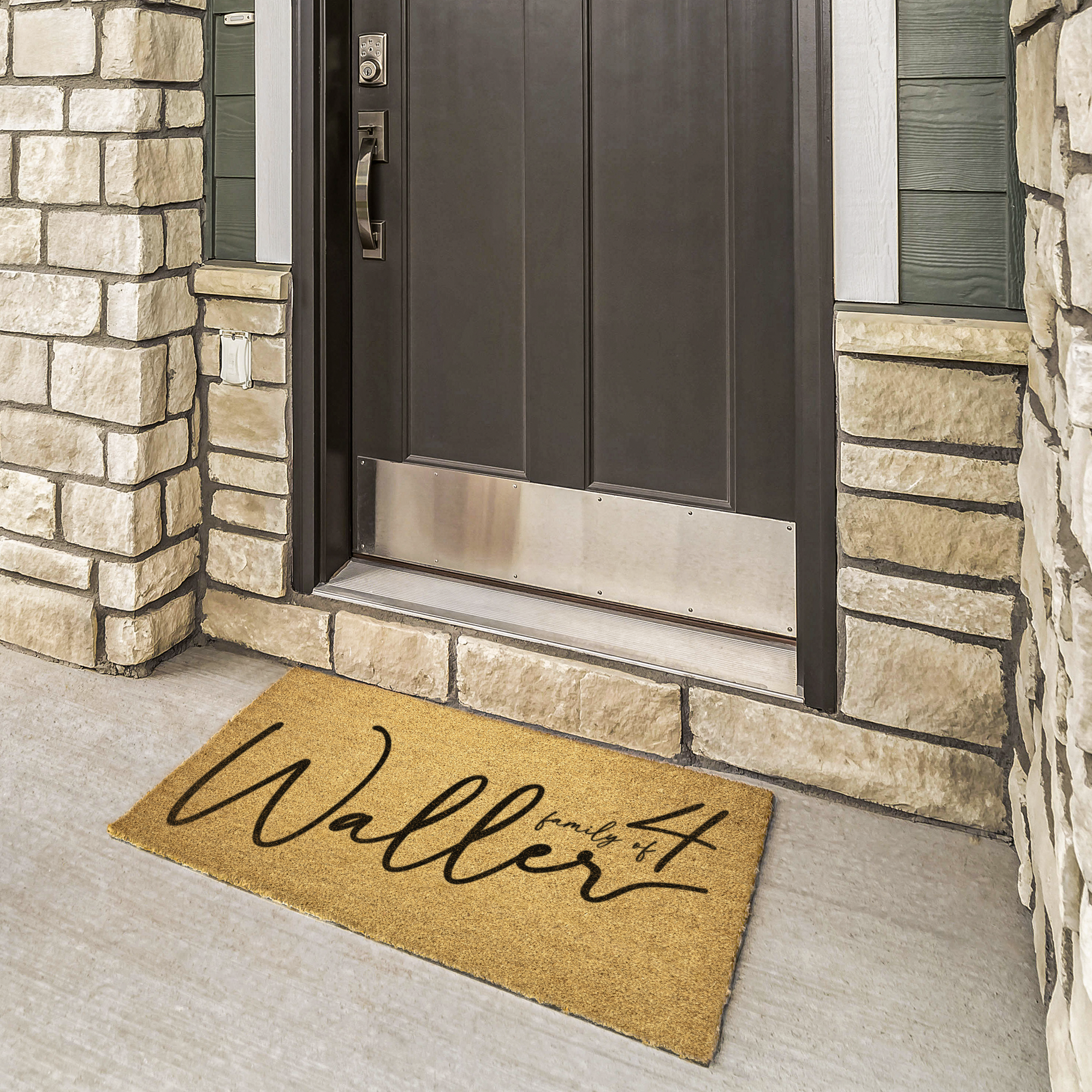 Personalized family coir welcome mat in black script at a bronze door framed by cream stone