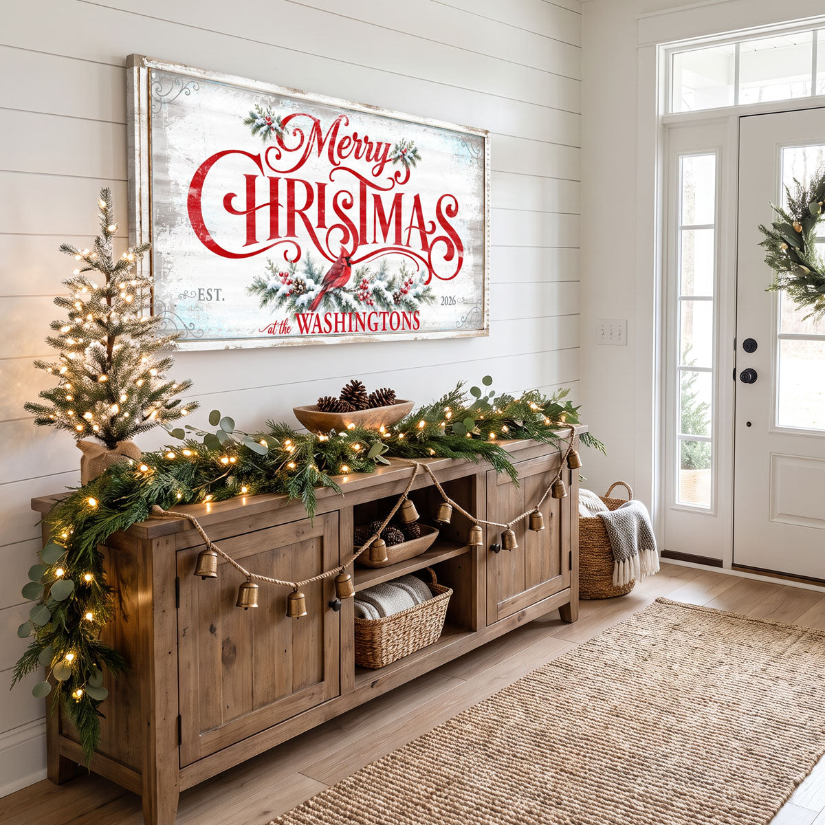 Personalized Merry Christmas sign in an entryway above a wood console with a lit garland and a wreath on the door