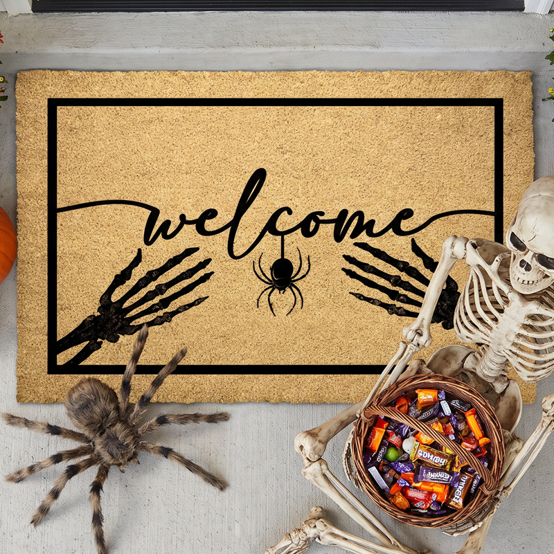 Skeleton doormat reading welcome with two skeleton hands and a hanging spider on natural coir