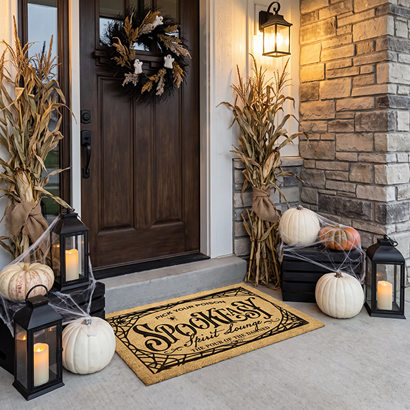 Spookeasy Lounge welcome mat on a porch with cornstalks, white pumpkins, lanterns and cobwebs