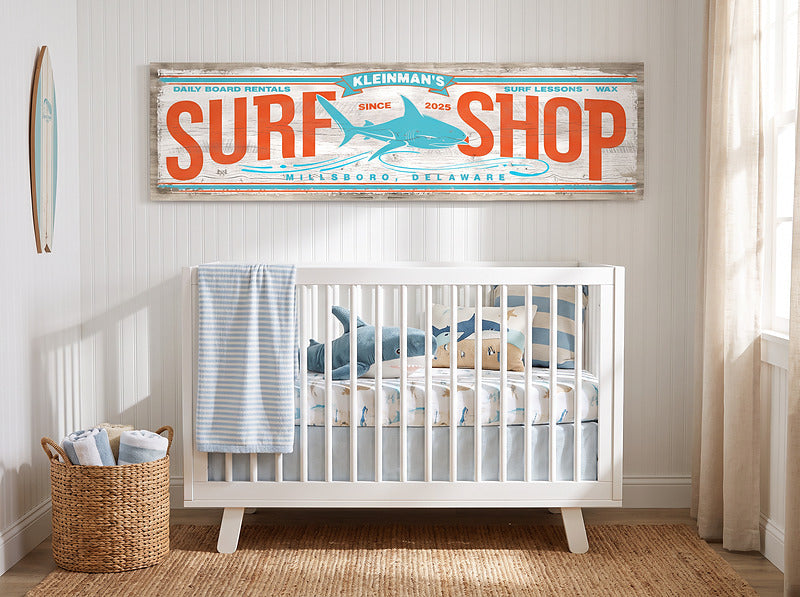 Surf nursery decor, personalized surf shop sign above a white crib with shark bedding and a jute rug
