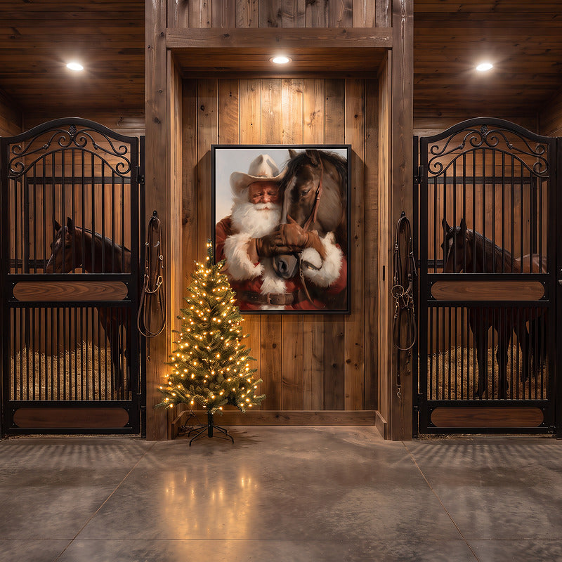 Western Santa and horse canvas in a black frame in a barn aisle between horse stalls with a small lit tree below